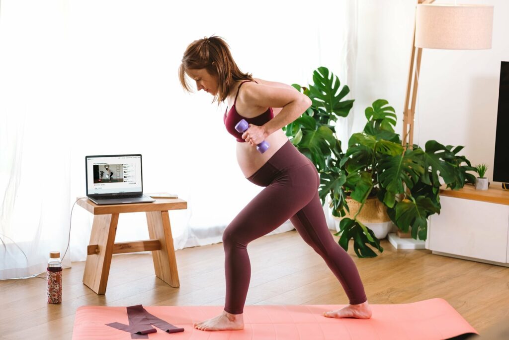 Femmes enceinte en train d'effectuer un mouvement sécurisé de fitness accompagnée via la plateforme WoMum Studio par une experte fitness spécialisée en accompagnement du sport pré et postnatal